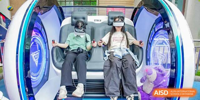 Two female students sitting in moving simulation chairs while wearing virtual reality (VR) headsets during a school event at Changsha WES (Bilingual) Academy.