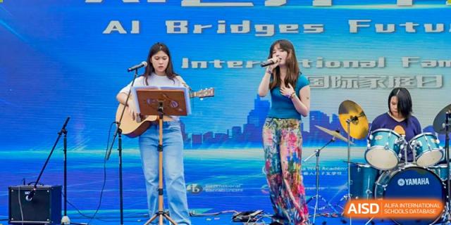 Two female students singing and playing the ukulele on a stage with a digital cityscape background at Changsha WES (Bilingual) Academy.