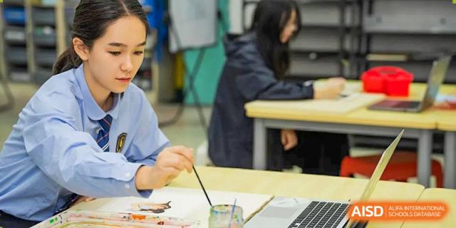 A high school student sitting at a desk and focusing on painting with a brush and watercolors in an art class at Changsha WES (Bilingual) Academy.