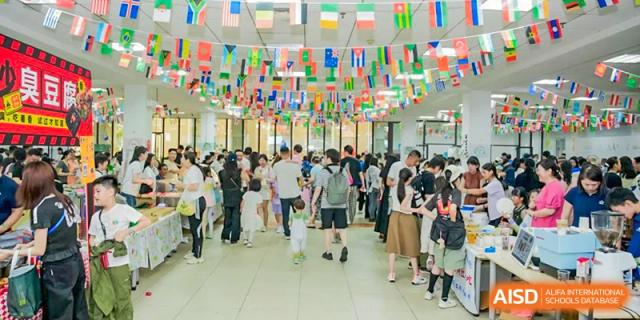 A large crowd of students, parents, and faculty mingling in the school hall under a decorative display of international flags for a cultural celebration at Changsha WES (Bilingual) Academy.