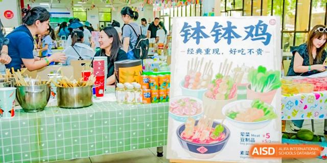 A close-up of a vendor stall selling traditional Chinese snacks like tanghulu (candied fruit skewers) and canned drinks at a school event at Changsha WES (Bilingual) Academy.