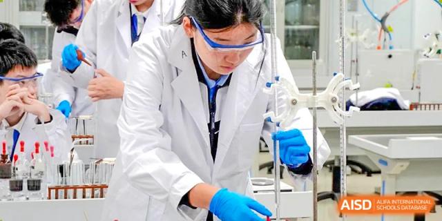 Student in a lab coat and safety goggles conducting a chemistry experiment at Shenzhen Third Senior High School International Division A-Level Class.