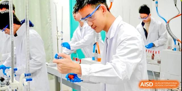 Male student in safety goggles and lab coat manipulating glassware for an experiment at Shenzhen Third Senior High School International Division A-Level Class.
