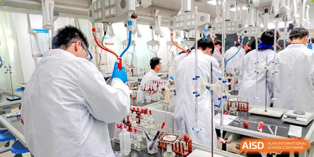 Students in lab coats working with complex chemistry equipment in a science lab at Shenzhen Third Senior High School International Division A-Level Class.
