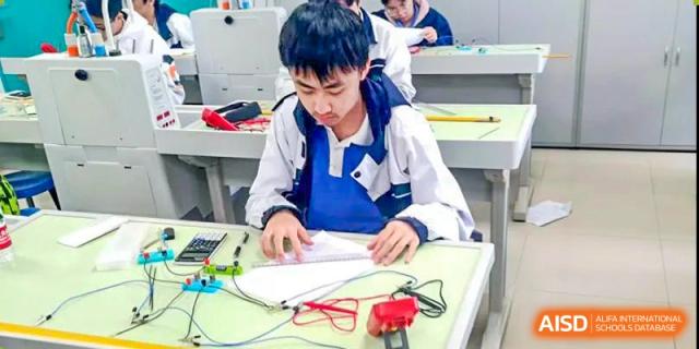 Student focused on writing or designing a technical project with wires and a multimeter on the desk at Shenzhen Third Senior High School International Division A-Level Class.