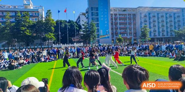 Wide shot of students participating in an outdoor group sports or performance event with school buildings in the background at Shenzhen Third Senior High School International Division A-Level Class.