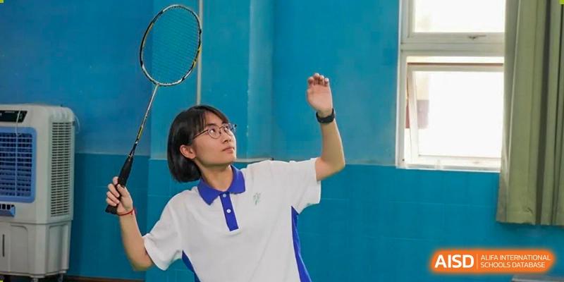 Student in a white and blue polo shirt and glasses raising their arm during an outdoor sports activity at Shenzhen Third Senior High School International Division A-Level Class.