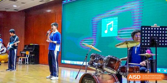 A student standing next to a drum set on a stage during a musical performance at Shenzhen Third Senior High School International Division A-Level Class.