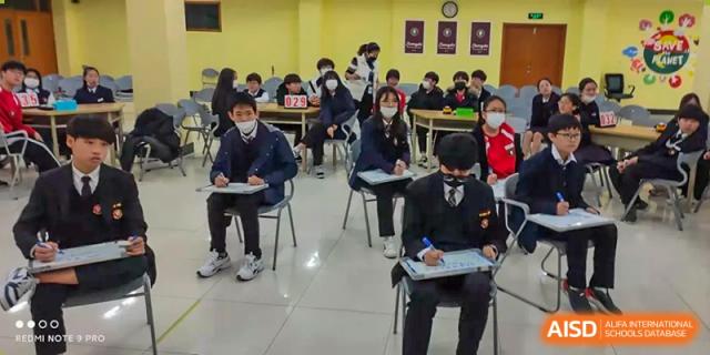 A group of students wearing school uniforms and masks, seated at desks and attending a lesson at Weihai Zhongshi Foreign School (WZFS).
