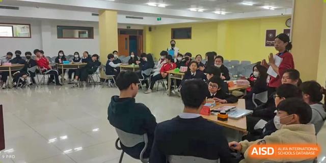 Weihai Zhongshi Foreign School (WZFS) students and a teacher participating in a group class or activity in a bright, indoor setting.