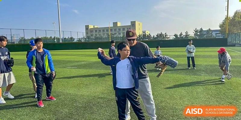 A student at Weihai Zhongshi Foreign School (WZFS) being guided by a teacher or coach during an outdoor physical activity on a sports field.