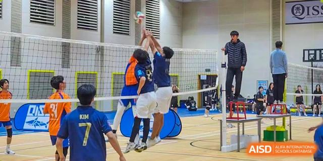 Students playing volleyball and jumping at a net indoors at Weihai Zhongshi Foreign School (WZFS).