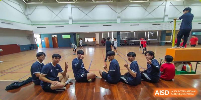 Students sitting and stretching during a physical activity or game indoors at Weihai Zhongshi Foreign School (WZFS).
