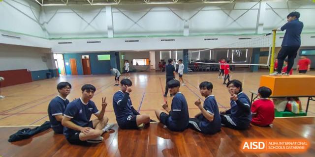 Students sitting and stretching during a physical activity or game indoors at Weihai Zhongshi Foreign School (WZFS).