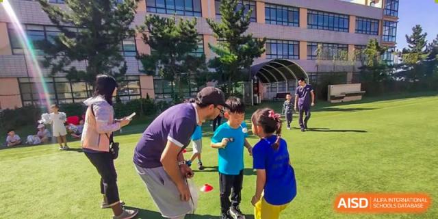 A teacher interacting with young students outdoors on the school grounds at Weihai Zhongshi Foreign School (WZFS).