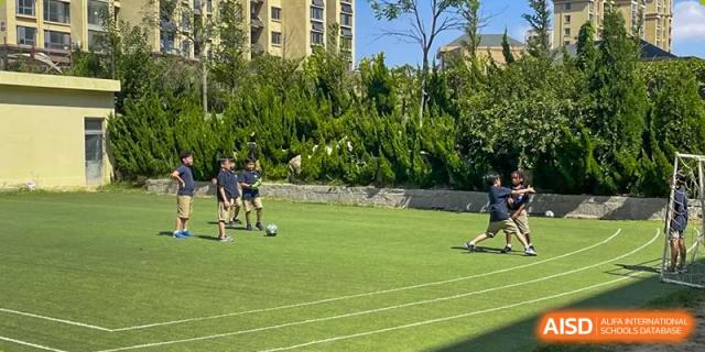Students playing soccer (football) on a green outdoor sports field at Weihai Zhongshi Foreign School (WZFS).