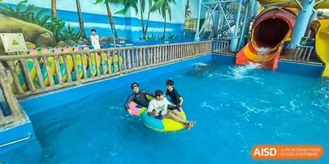 Students enjoying an aquatic activity in a swimming pool or water park area on inflatable tubes at Weihai Zhongshi Foreign School (WZFS).