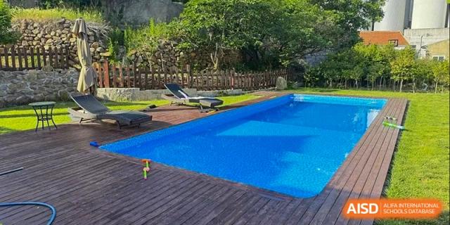 An outdoor swimming pool area with a wooden deck surrounded by trees at Weihai Zhongshi Foreign School (WZFS).