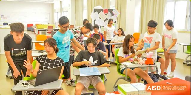 A group of students collaborating on a project, with one student playing a small keyboard instrument at Alcanta International College.