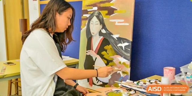 Students looking at and working on an art project, possibly a painting or drawing, at Alcanta International College.