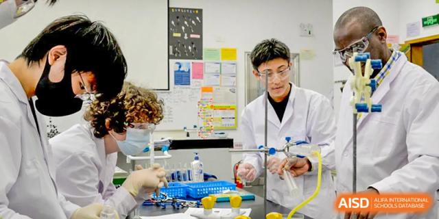 A student in a lab coat and safety glasses performing a chemistry experiment with beakers and flasks at Alcanta International College.