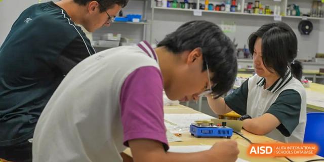 A student in a pink shirt leaning over a desk, focused on a project or assignment at Alcanta International College.