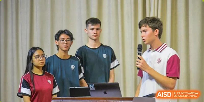 A male student standing at a podium with a laptop, possibly giving a presentation at Alcanta International College.