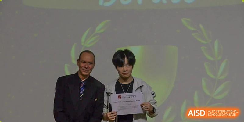 A student smiling while receiving an award or certificate from a teacher at Alcanta International College.