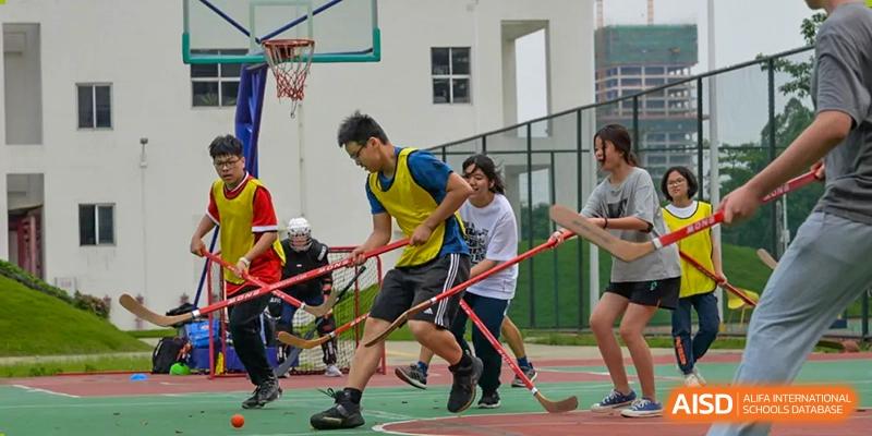 Students playing floorball outdoors with sticks on a court at Alcanta International College.