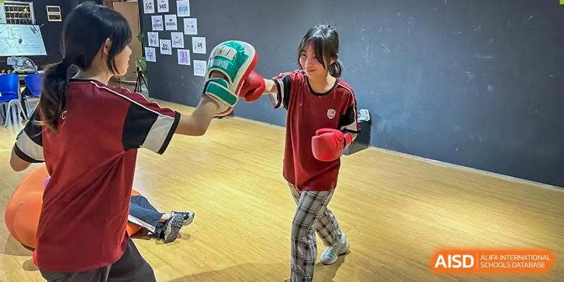 A student wearing boxing gloves and punching a bag during a physical education class at Alcanta International College.