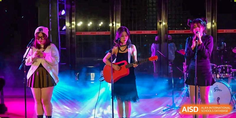A female student playing an acoustic guitar and singing on a stage with vibrant lighting at Alcanta International College.