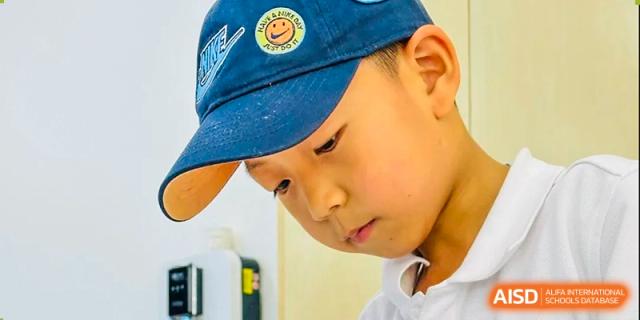 A young male student from Changsha BeeMee Forest School (CBFS) wearing a baseball cap and intently focused on a desk activity.