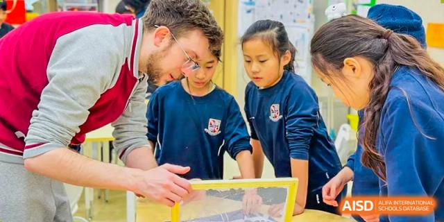 A foreign teacher at Changsha BeeMee Forest School (CBFS) working closely with two students on a project board.
