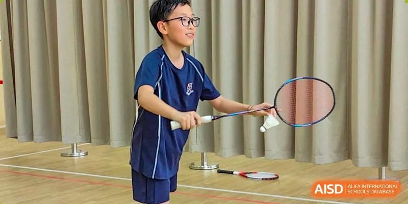 A male student from Changsha BeeMee Forest School (CBFS) practicing badminton indoors, holding a racket.