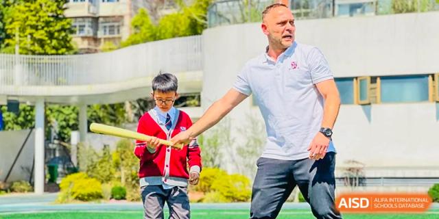 A teacher from Changsha BeeMee Forest School (CBFS) guiding a young student in an outdoor physical activity, holding a red and yellow baton.