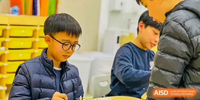 A male student from Changsha BeeMee Forest School (CBFS) wearing glasses and intently focused on a desk-based activity, possibly Go or Chess.