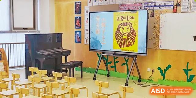 A classroom at Changsha BeeMee Forest School (CBFS) featuring small wooden chairs, an interactive whiteboard displaying a poster for 'Le Roi Lion' (The Lion King).