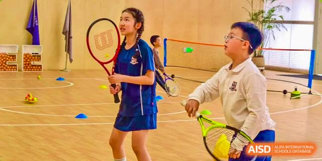A student from Changsha BeeMee Forest School (CBFS) holding a badminton racket during indoor sports practice.