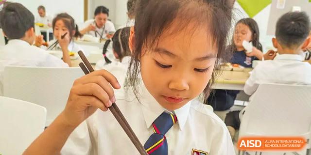 A female student from Changsha BeeMee Forest School (CBFS) in uniform, looking at her food while holding chopsticks.