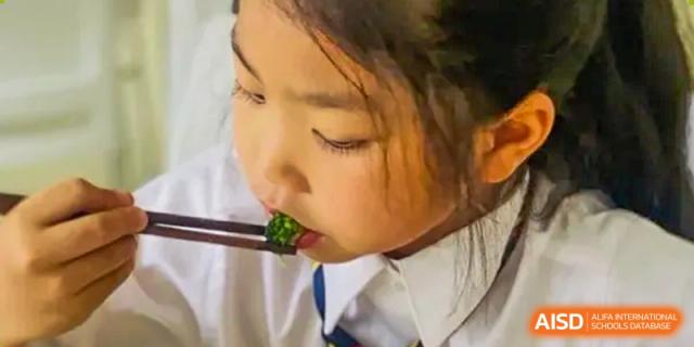 A close-up of a young female student from Changsha BeeMee Forest School (CBFS) eating a piece of broccoli with chopsticks.
