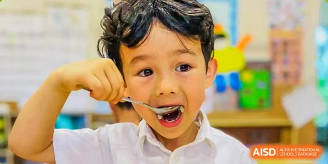 A young male student from Changsha BeeMee Forest School (CBFS) with wide eyes, eating with a spoon.