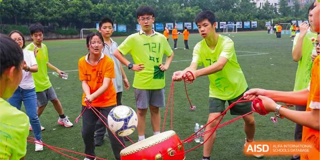 CHONGQING WEIMING SCHOOL students playing a teamwork game involving a soccer ball and a large drum on a rope setup.