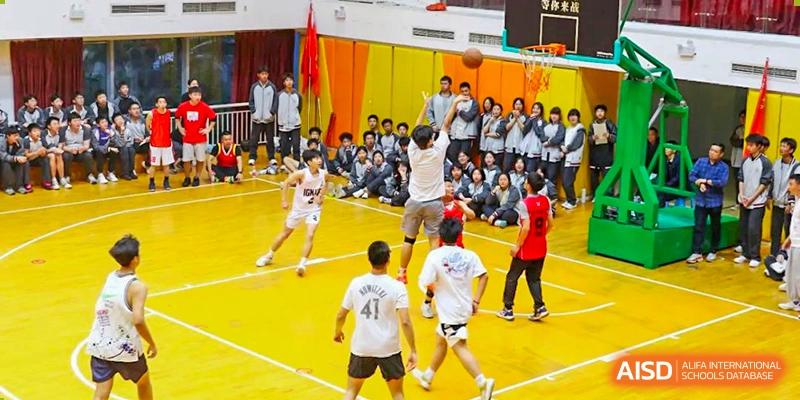 CHONGQING WEIMING SCHOOL students playing basketball on the court with many classmates watching in the stands.