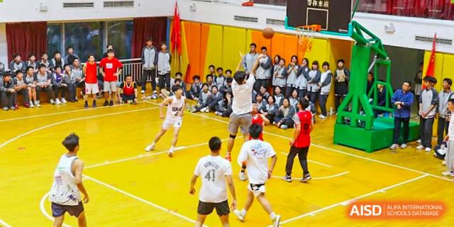 CHONGQING WEIMING SCHOOL students playing basketball on the court with many classmates watching in the stands.