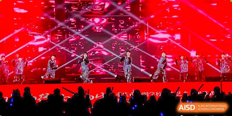 A student or performer from CHONGQING WEIMING SCHOOL singing on a stage with bright red and black lighting during a school event or concert.