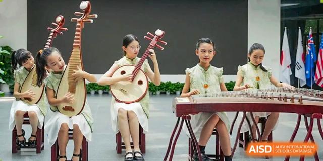 Two CHONGQING WEIMING SCHOOL students performing traditional Chinese music, one playing the Pipa and the other the Guzheng, on stage.