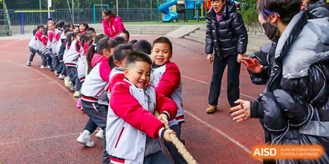 A group of younger CHONGQING WEIMING SCHOOL students smiling while participating in a game of tug-of-war.