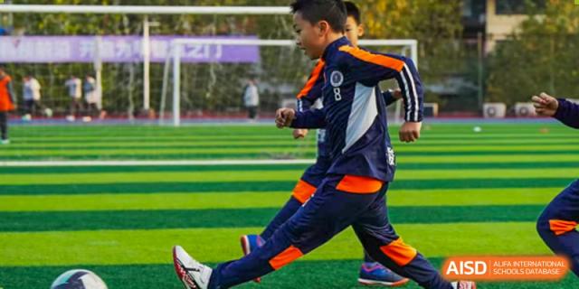 Two CHONGQING WEIMING SCHOOL students competing in a dynamic football (soccer) drill or practice on an artificial turf field.