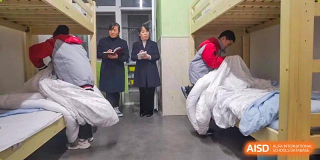Two female CHONGQING WEIMING SCHOOL staff members or teachers conducting a dormitory check or inspection of a student's living area.