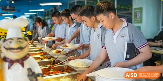 A line of CHONGQING WEIMING SCHOOL male students wearing school uniforms serving themselves food in the cafeteria or dining hall line.